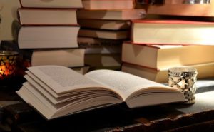 大量の重ねられた本の前に1冊のひかられた書籍、2020年4月25日(土)に開催する東京読書交換会vol.102の広報、書籍の右隣りに青・白の小さな装飾ランプ、読書会@オンライン(記事内挿入画像)